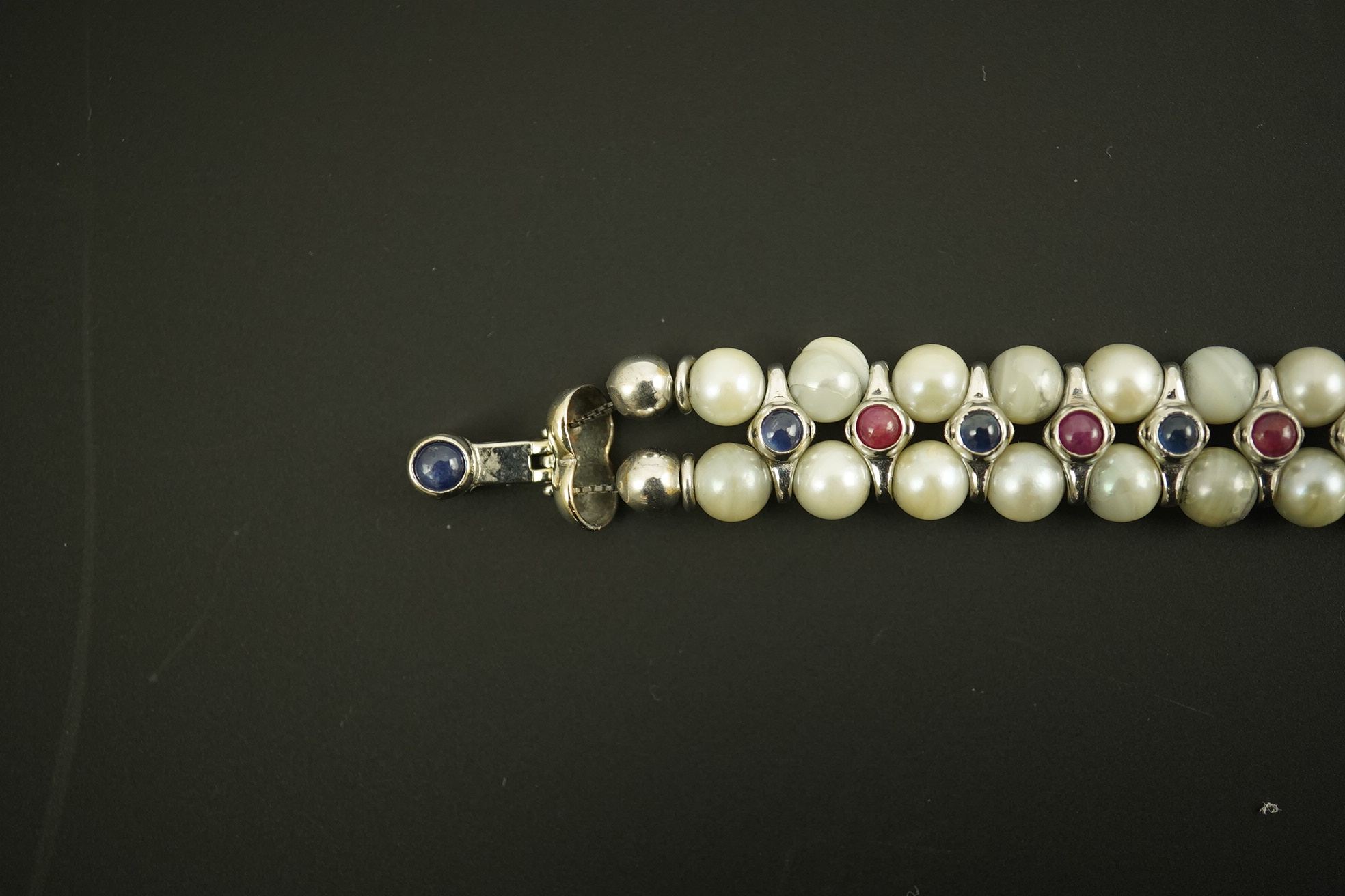 A late 20th century 18k white gold and two row cultured pearl bracelet, set with single row of cabochon rubies and sapphires